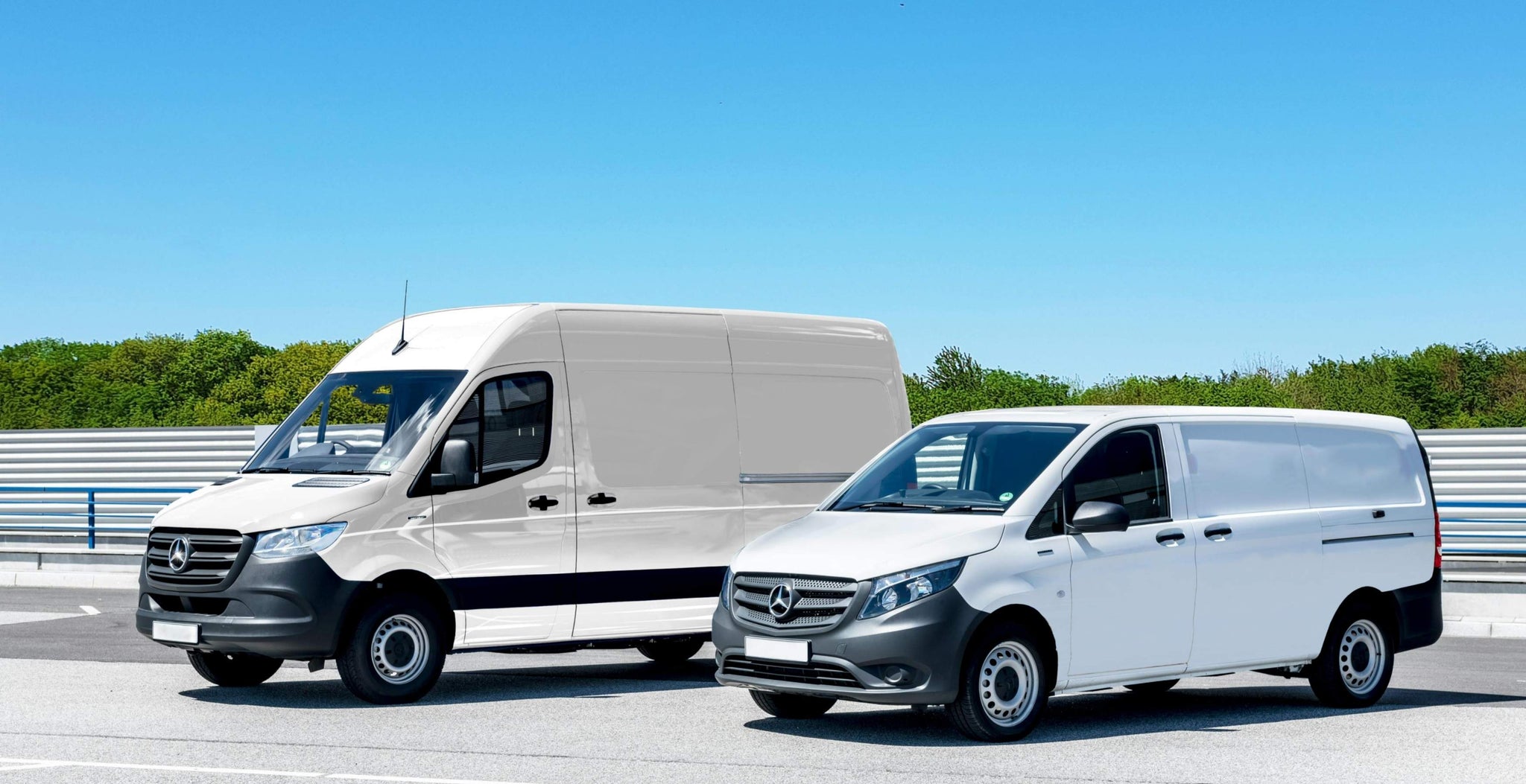 Two Mercedes-Benz vans on a road with a clear blue sky and greenery in the background.
