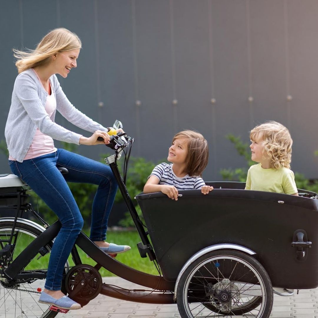 Woman riding a bicycle with her two child in a cargo bike trailer