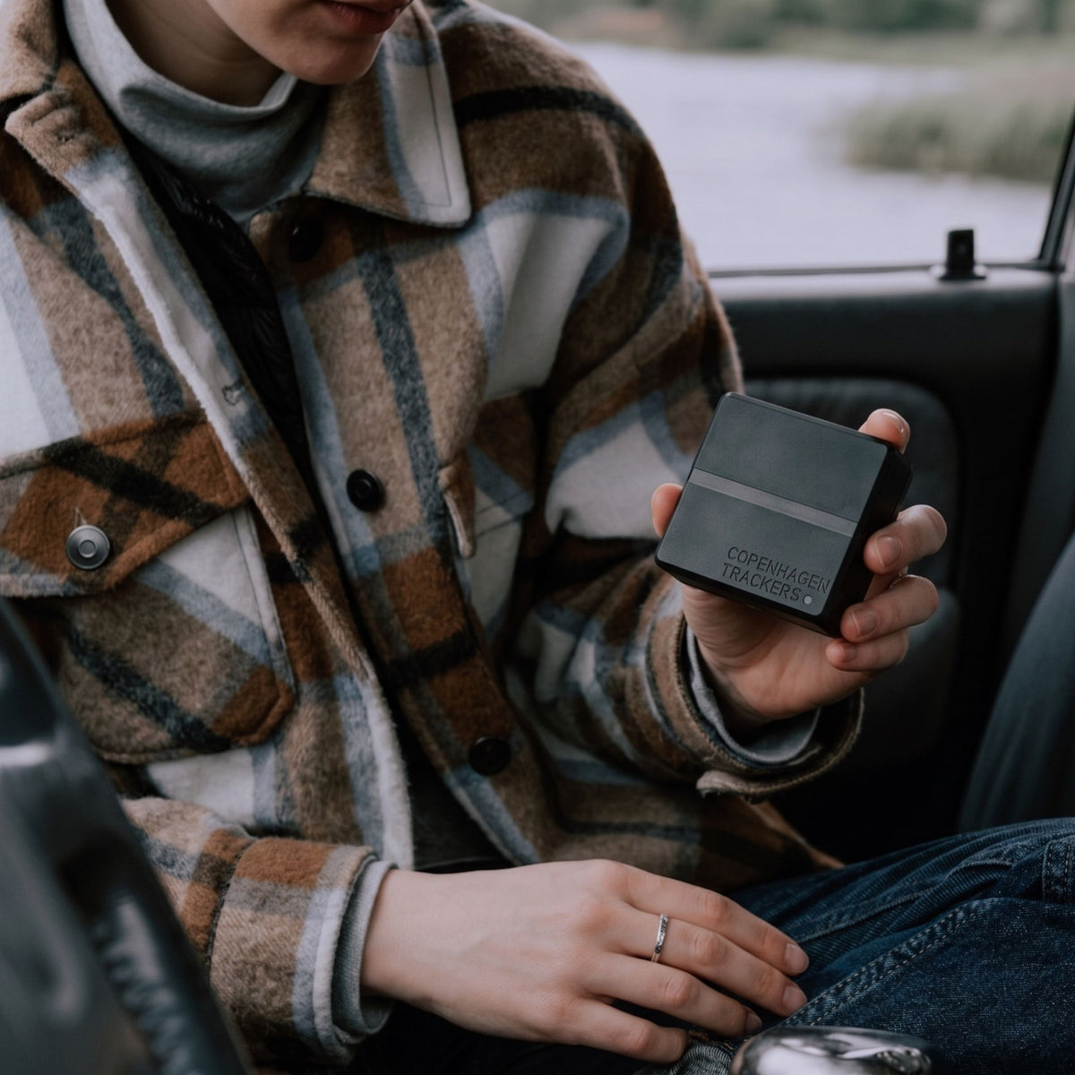 Person holding the Cobblestone 2.0 GPS tracker, sitting inside a vehicle.